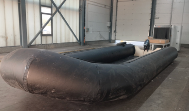 Large black inflatable boat with a motor inside a warehouse with concrete floor and industrial walls.
