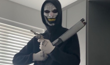 Nikolli in a black hoodie, covering his face with a face mask and holding two firearms