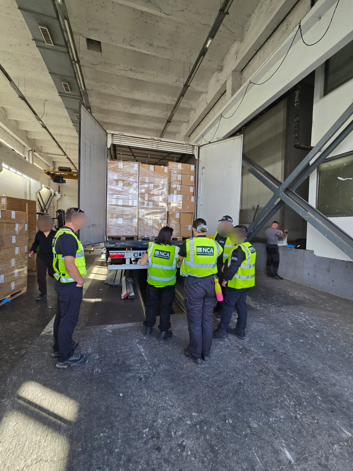 Officers in hi-vis searching a lorry in a warehouse