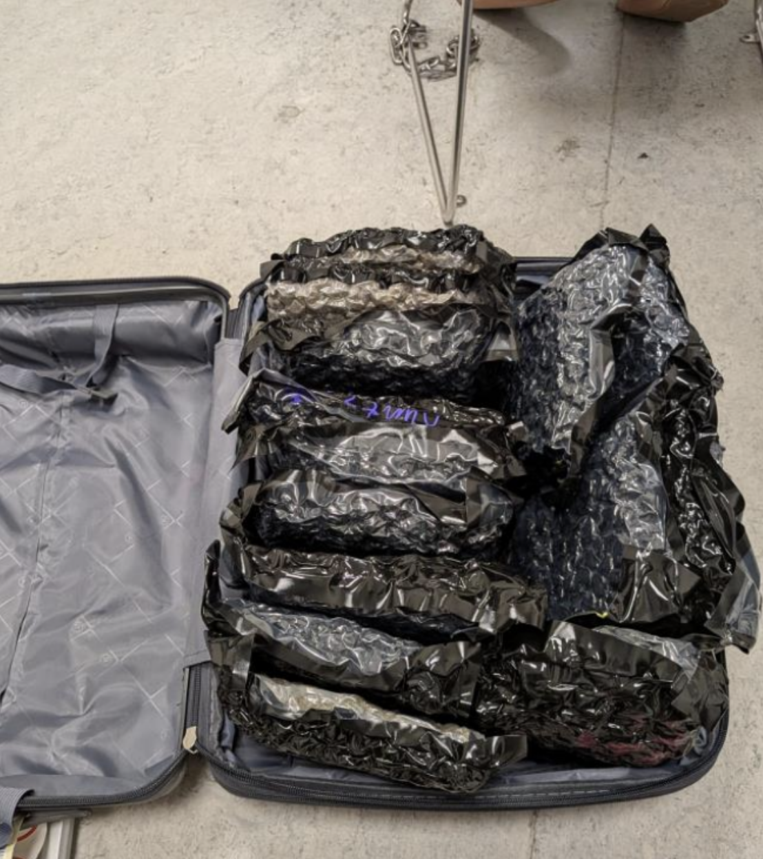 Open suitcase filled with multiple black bags of cannabis tightly packed inside on a concrete floor